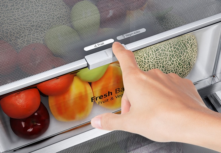 Hand adjusting fridge drawer selector for "Fruit" and "Vegetables" with tomatoes, peppers, and a melon inside.